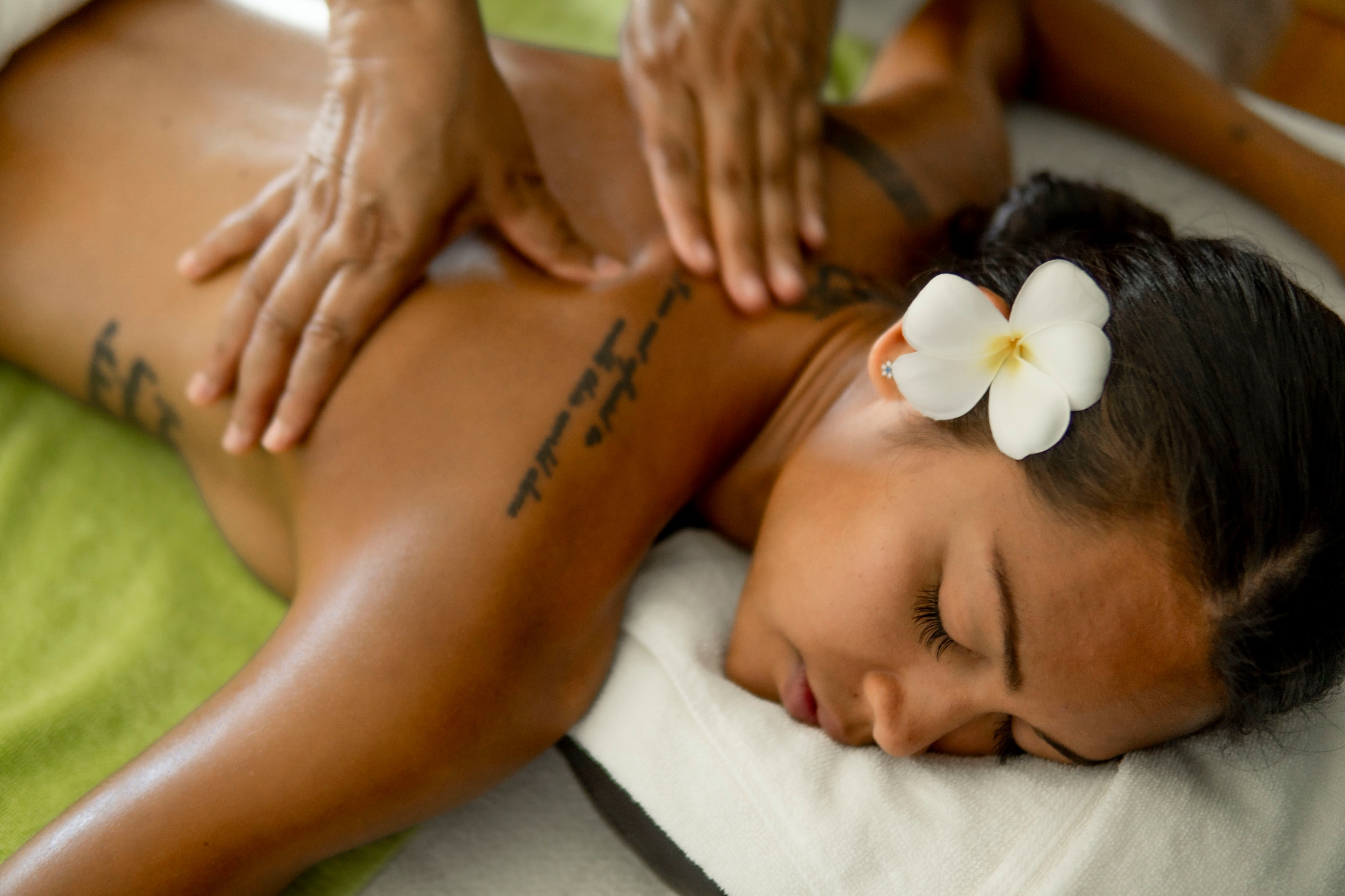 A therapist's hands massaging a guest's back, a frangipani flower in her hair