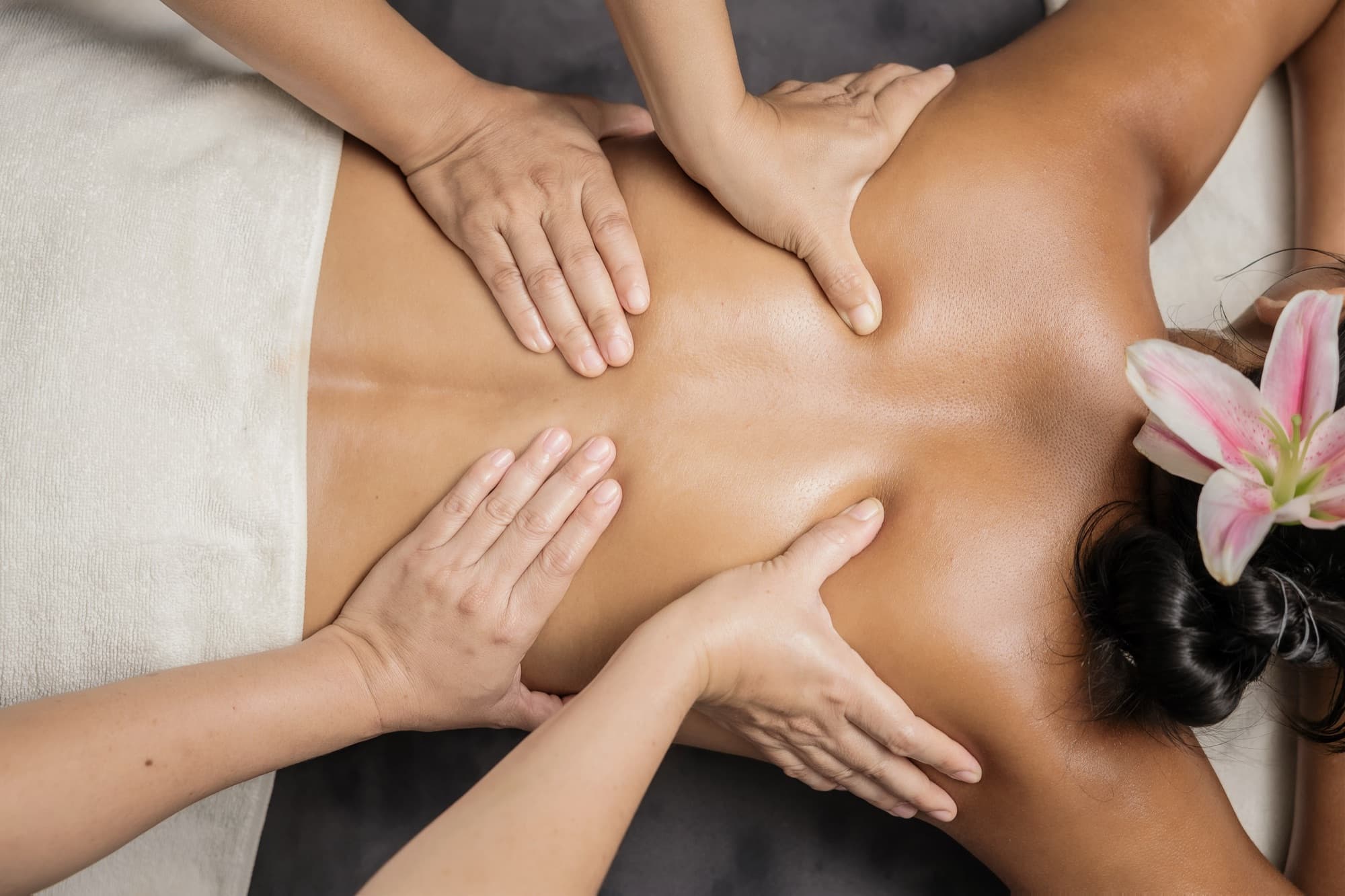 A four-hands massage seen from above, a lily in the guest's hair